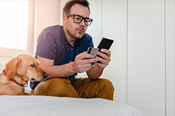 man sitting down looking at his cell phone with dog beside him