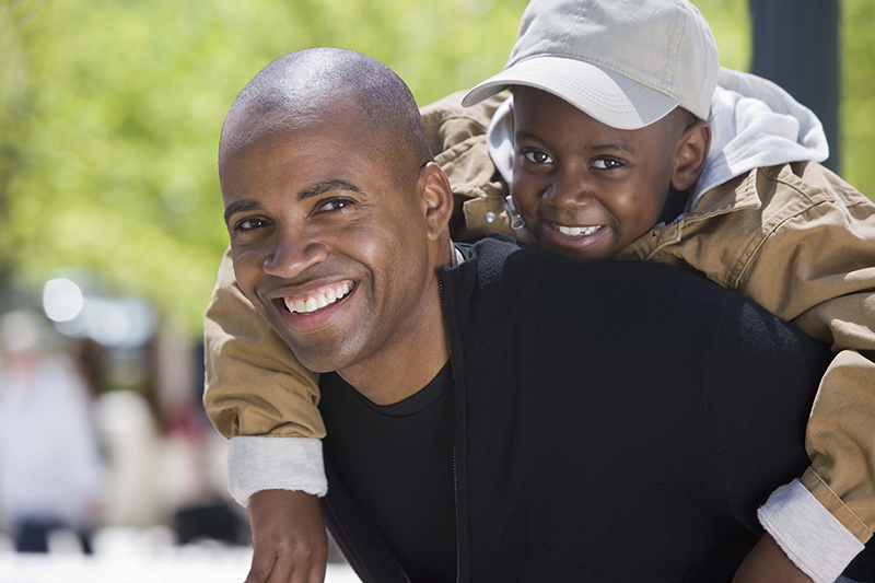 man with young kid on back looking at camera and smiling
