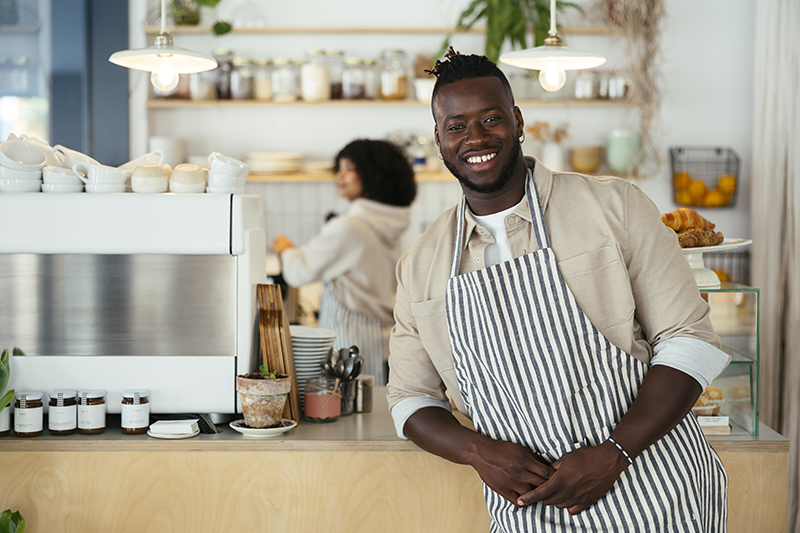 man at coffee shop wearing apron and leaning on counter