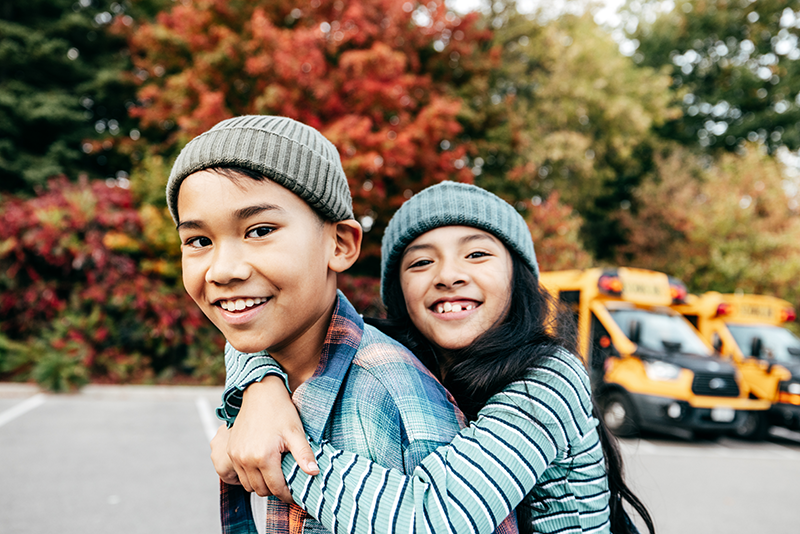 two children hugging and looking at the camera with a bus in the background