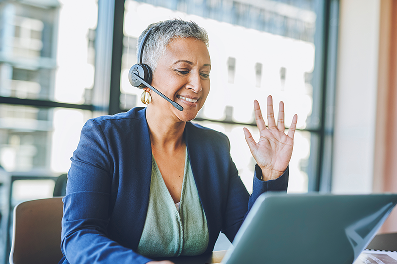 woman sitting at computer with headset on waving at the screen