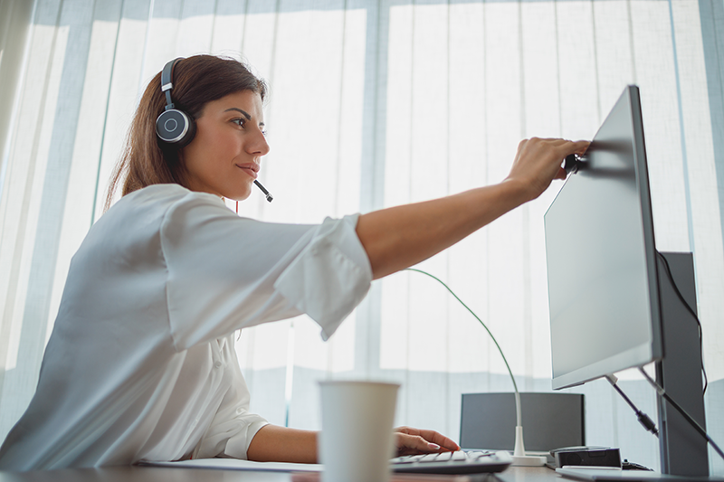 woman sitting at computer adjusting camera for video call