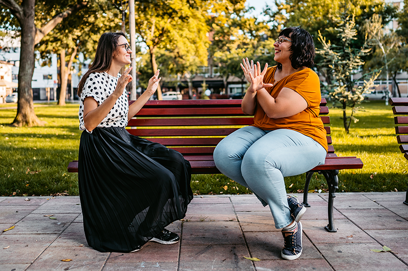 two women sitting on park bench communication with sign language