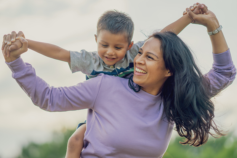 woman smiling and holding hands with young boy riding on her back